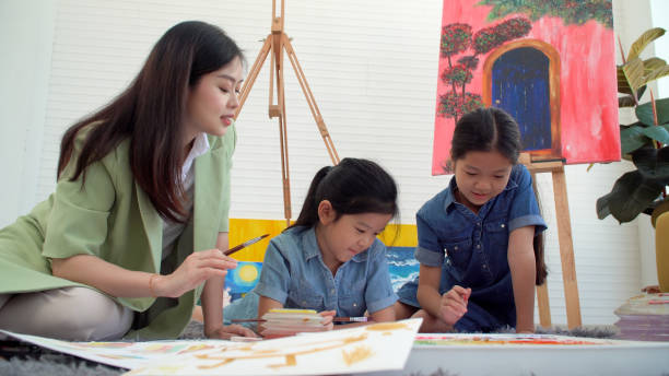 istock Asian two siblings learning study watercolor paint together at home. Teacher or parent teach student or daughter drawing paint color imagination on paper homework.Activity creativity education concept 1409066708