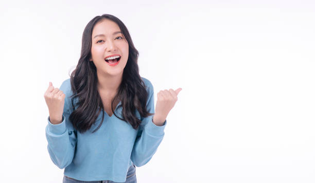 istock Joyful asian woman successful with excitement up keeps hands raised arm standing on white background with copy space. Excited young girl screaming success holding fist up looking camera over isolated. 1409066775