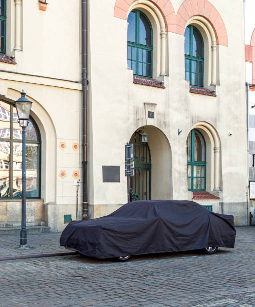 istock Car covered with a black cover on tiled road. Modern architecture. 1409069493