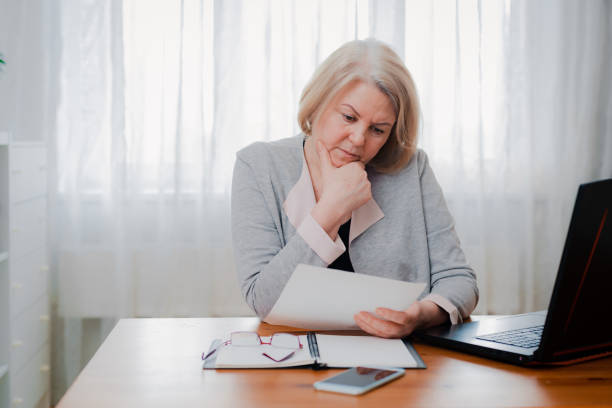 istock older Senior woman struggles at the computer with paper documents, puzzled by the business decision 1409069868