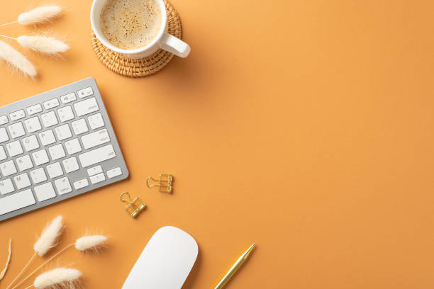 istock Business concept. Top view photo of workspace white keyboard computer mouse gold pen binder clips cup of hot drinking on rattan serving mat and white lagurus flowers on isolated orange background 1409070687