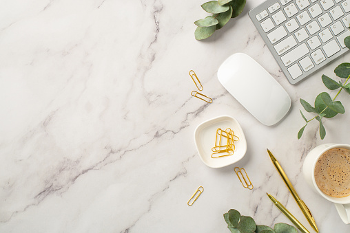 Business concept. Top view photo of workspace white keyboard computer mouse stationery gold pens clips cup of hot drinking and eucalyptus on white marble background with copyspace