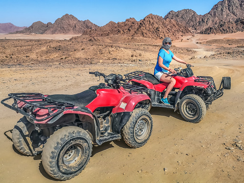 Young adult girl dressed in arafatka on a quad bike in the Echo Valley near Sharm El Sheikh, Egypt. Tourist attraction in the Sinai desert