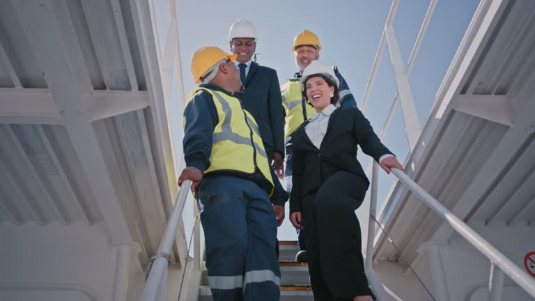 Diverse group of marine engineers and managers wearing safety hardhats while discussing construction work on deck at sea. Technician and corporate contractors walking down steps to survey cargo ship