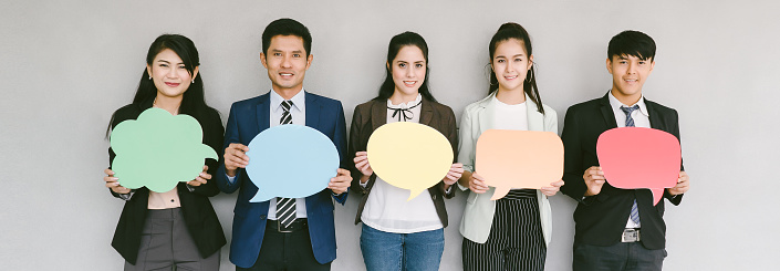 Group of business people while holding up speech bubble icons on gray banner background. wide crop