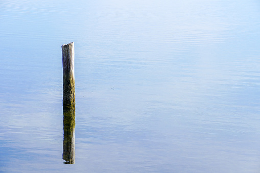 A beautiful shot of a calm seascape with a broken pillar sticking out of the water on the horizon background.\nD.H