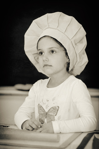 Portrait of cute, adorable little girl practicing to be a chef in kindergarten. Sepia photography. Little cooker