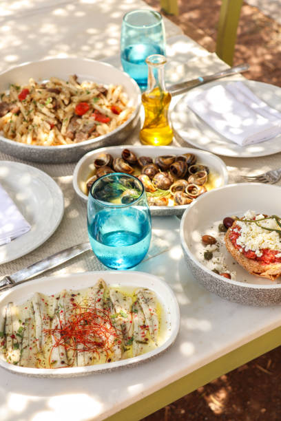 ギリシャのディナーテーブル、クレタ島の珍味が入ったオリーブの木の下の食べ物とプレート - gourmet snail food escargot ストックフォトと画像