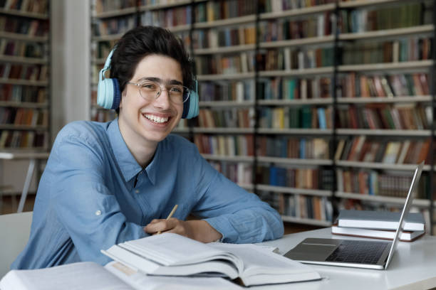 istock Happy student guy in headphones sit at table in library 1409086742
