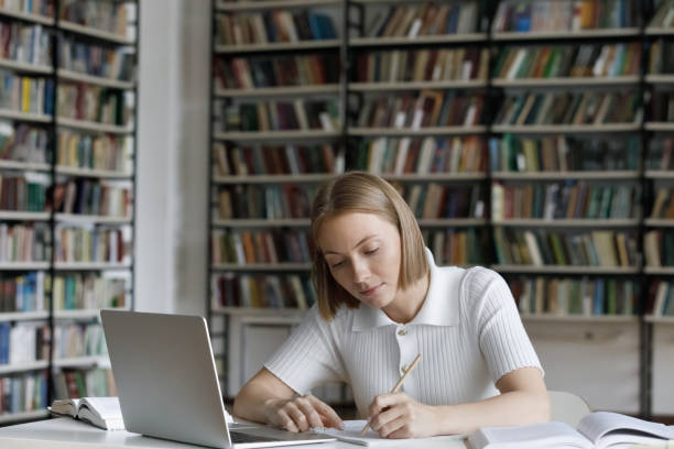istock Student prepare for test writing in copybook sit in library 1409086747