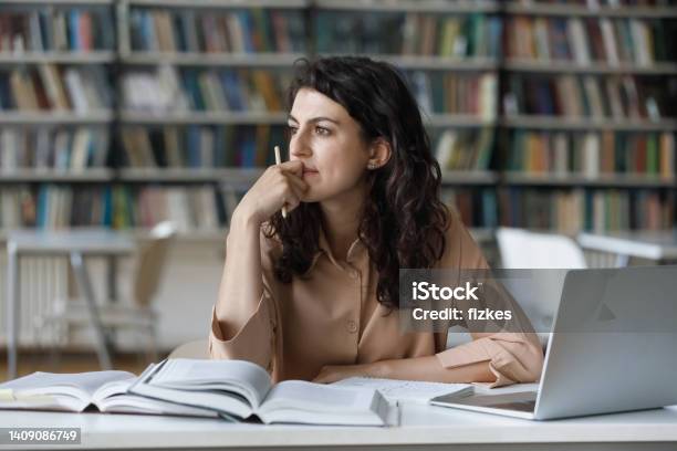 Thoughtful Girl Studying In Library Seated At Table With Textbooks Stock Photo - Download Image Now