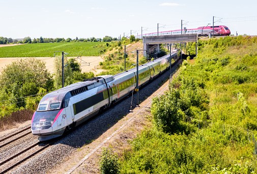Claye-Souilly, France - July 4, 2022: A TGV Inoui and a Thalys high-speed trains pass one above another in the countryside on a sunny day.