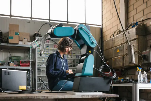 female technician programs a robot arm with a digital tablet