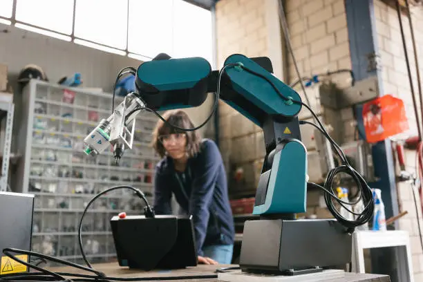 female technician programs a robot arm with a digital tablet