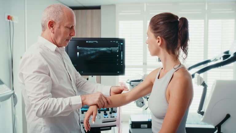 Physiotherapist uses ultrasound technology to examine an athletic elbow joint injury. A doctor examines a female patient with a machine to scan for ligament muscle damage in a medical facility