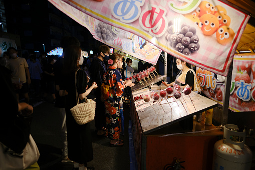 Kyoto, Japan - July 16, 2022: A woman serves candy apples at a food stall at the Gion Festival. The return of festivals like this has been a boon for food stall workers who have been hit hard by the pandemic.