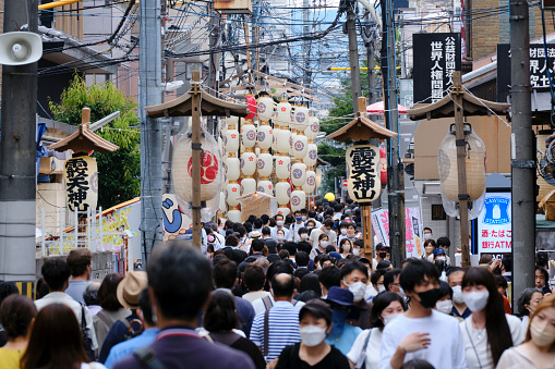 Kyoto, Japan - July 16, 2022: Festival goers slowly walk along a narrow street in downtown Kyoto to view the ceremonial yamaboko floats. The following day, the floats file onto Shijo Street to begin a parade.