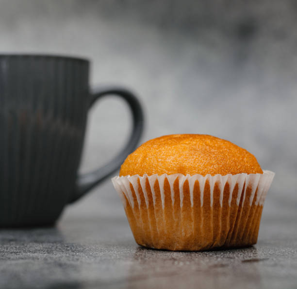 istock Bright brown cupcake and behind a cup of coffee on a gray background. 1409096723