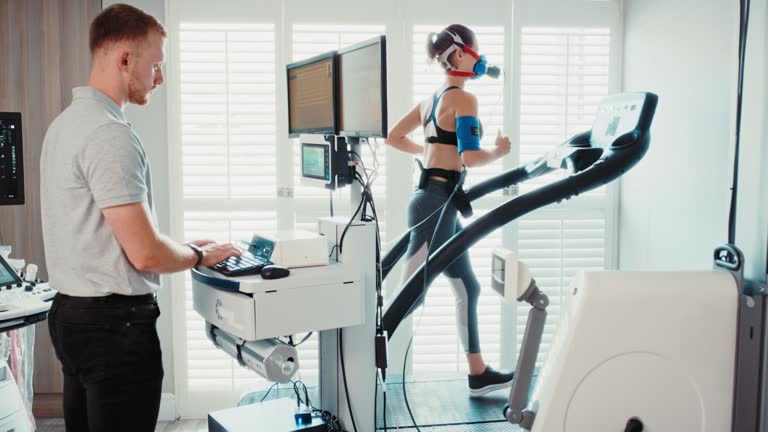 Sports scientist performing metabolic gas analysis test on an athlete in centre. Fit, active, healthy, athletic woman wearing mask, running on treadmill for breathing test. Aerobic sports performance