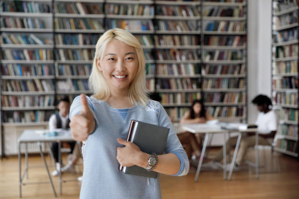 istock Asian student girl pose in library showing thumb up sign 1409098800