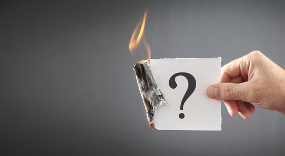 Male hand showing burning paper with a question mark.