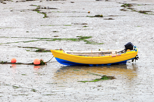 Small yellow and blue rowing boat with outboard motor resting on mud at low tide