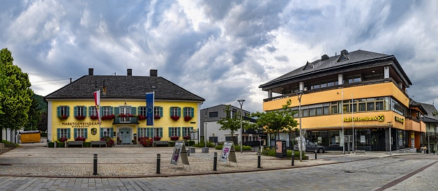Altmünster, Austria, July 9, 2022: Panoramic view of the town hall (left) on the main square in the village of Altmünster on the shore of the lake Traunsee in Upper Austria under cloudy sky.