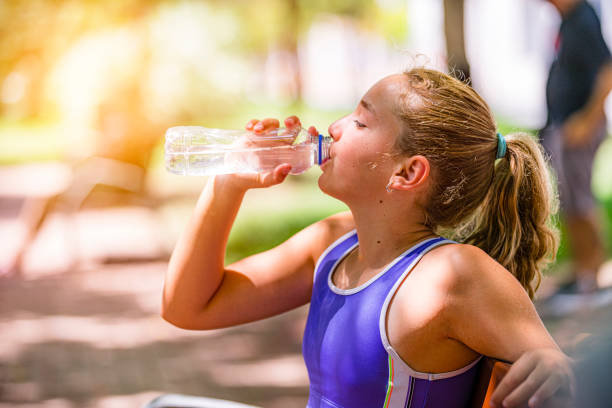 Side view of a little girl drinks sparkling water from a glass at a beach bar on a summer day