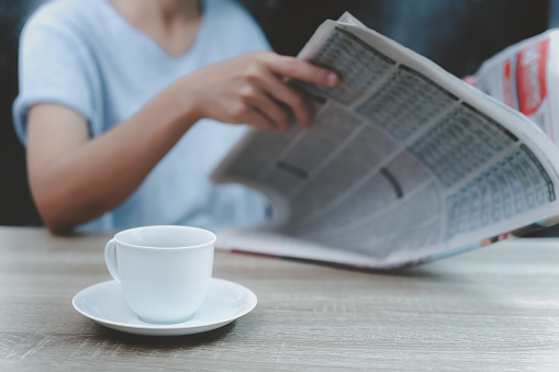 A cup of coffee and woman read newspaper.