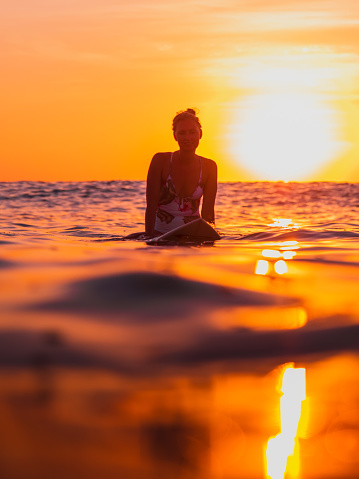 Attractive surfer woman on a surfboard in ocean with sunset or sunrise tones.