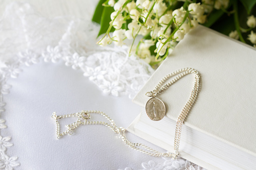 First Holy Communion with sacred medal on chain and flowers, concept background religion