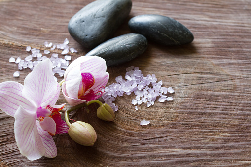 Bath salt, orchid and massage stones on wooden background, spa concept beauty