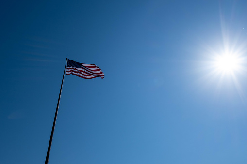The Flag of United States flutters in front of the sun.