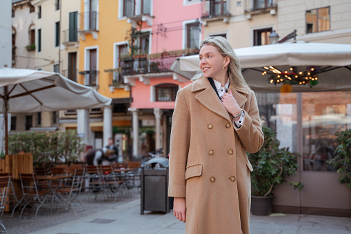 Smiling contented stylish blonde woman standing in the street outside the cafe and looking aside