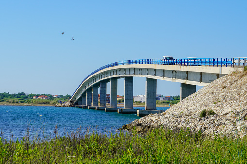 Drone image of Fjordforbindelsen, a new bridge over Roskilde Fjord on the major island Sjælland (Zealand) in Denmark. Dramatic cloudscape and lens flare in background over the bridge and sea.