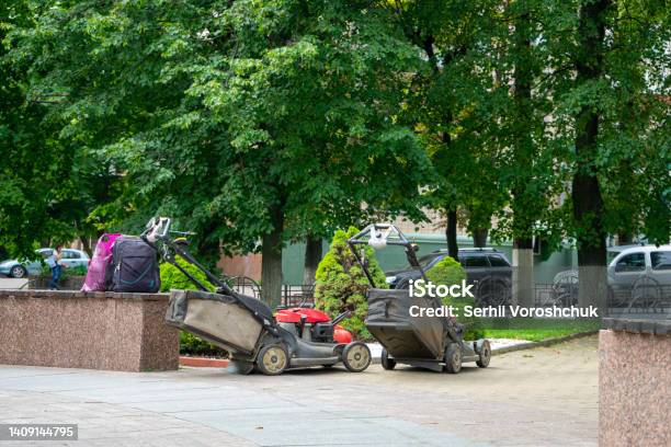 Two Lawn Mowers Stand On The Street In The City Stock Photo - Download Image Now - Branch - Plant Part, City, City Life