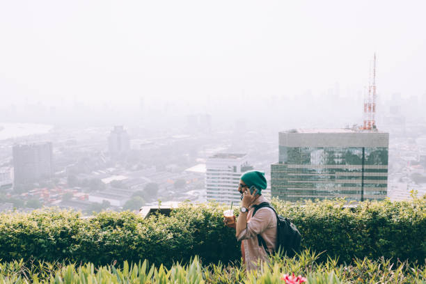 A happy Indian hipster with glasses and a green beanie using his smartphone and drinking coffee  while relaxing outdoors.