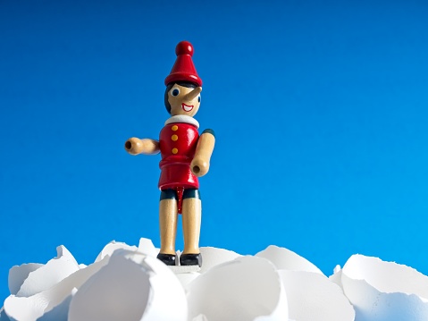 A small wood character walks on egg shells. the wood Pinocchio toy balances on eggs with a blue sky background. a metaphor for using extreme caution as to walk on eggs.