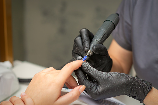 Manicurist elimina el esmalte de uñas utiliza la máquina eléctrica de la lima de uñas durante la manicura en un salón de uñas. photo