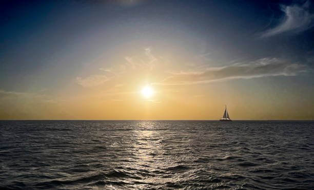 profitez d’une croisière au coucher du soleil en regardant un coucher de soleil sur la mer des caraïbes près d’aruba avec un voilier solitaire à l’horizon - sailing sailboat sunset aruba photos et images de collection