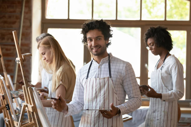 istock Painter man holding palette and paintbrush posing in art studio 1409155371