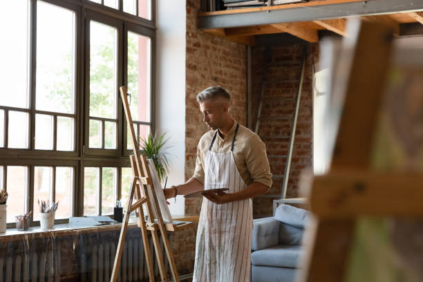 istock Serious man painter holds palette and paintbrush drawing on canvas 1409155391