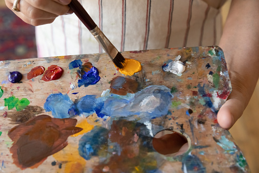 Unrecognizable older painter female hands hold wooden palette and paintbrush, close up cropped view. Creative hobby, professional occupation, activity for soul, improve talent and skill, craft concept