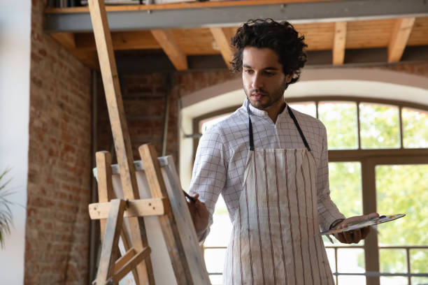 istock Young handsome painter man painting pictures on canvas 1409155401