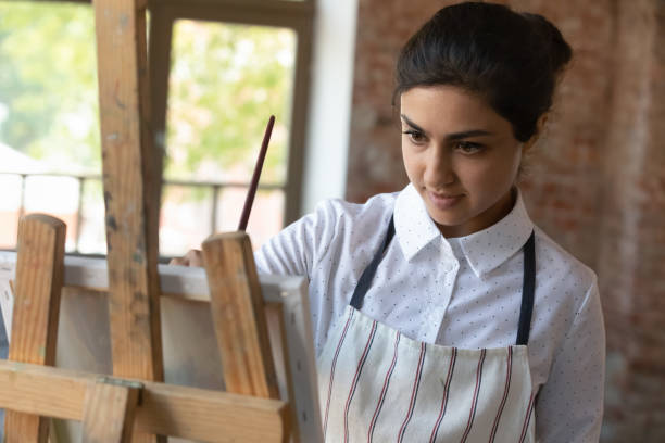 istock Attractive Indian woman painter holds paintbrush drawing on canvas 1409155409
