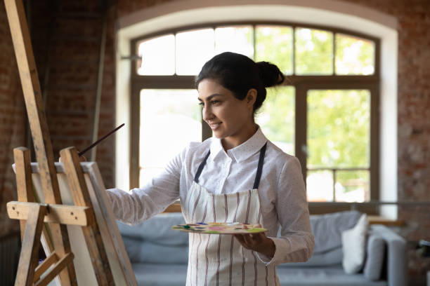 istock Indian woman painter drawing with paints on canvas in workshop 1409155411