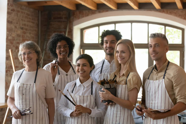 istock Group of people holding paintbrushes pose in art studio workshop 1409155415