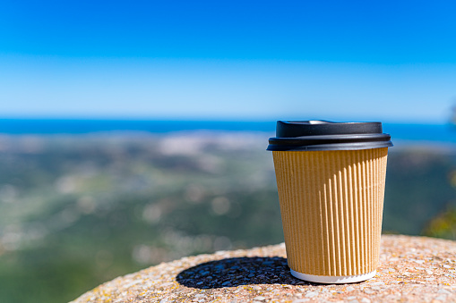 Close up view of a disposable coffee cup with lid shot on stone outdoors. Selective focus on cup. High resolution 42Mp outdoors digital capture taken with SONY A7rII and Zeiss Batis 40mm F2.0 CF lens