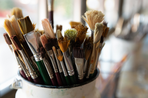 Close up bunch of used and cleaned diverse shapes and size, natural bristle paintbrushes in bucket, tools, supplies for artists after art-class. Creative hobby, painter equipment background concept