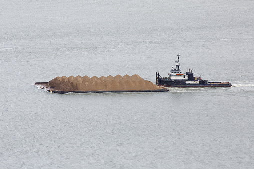 Martinez, Calfornia / USA - February 15 2021: An image of a tug boat pushing a dredge bard which is filled with soil.